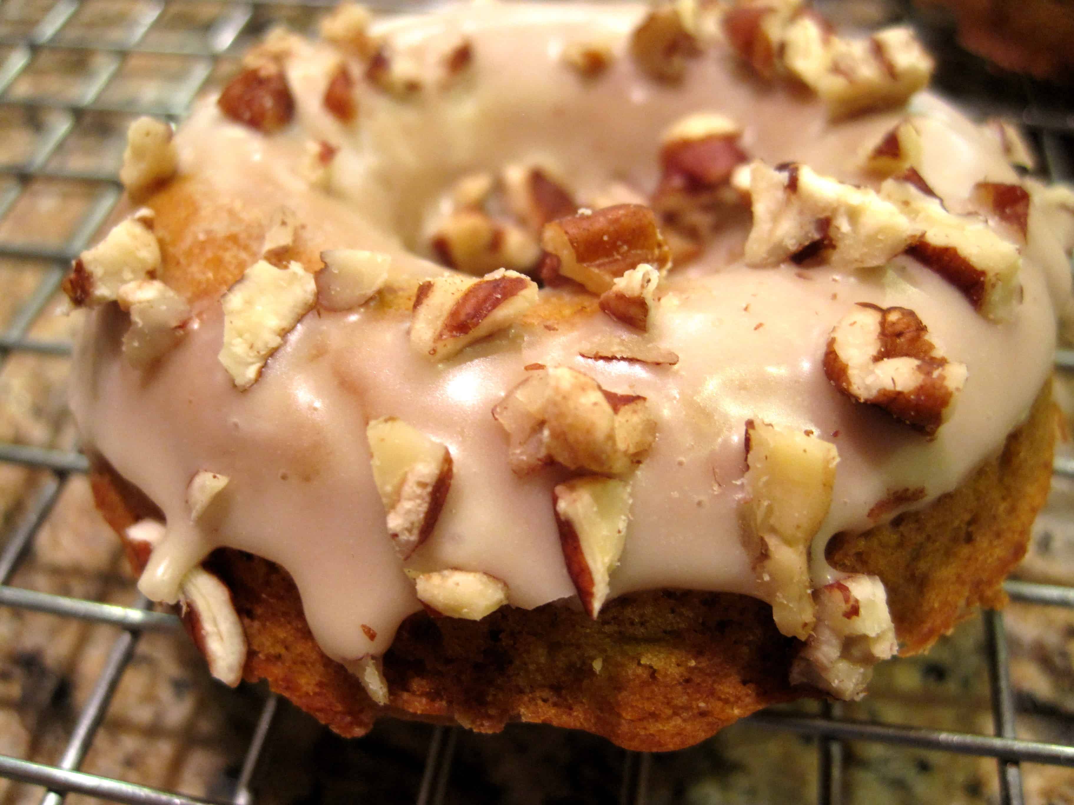 A freshly-glazed baked pumpkin donut on a metal rack.