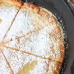 A sliced oven pancake in the pan covered in powdered sugar.