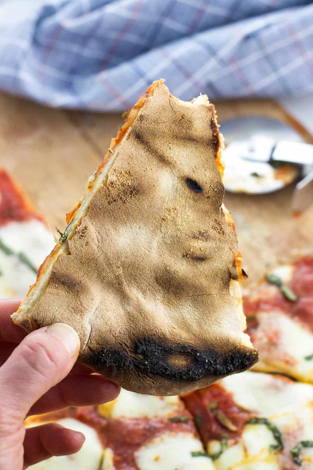 The bottom of a slice of pizza being held up to show the crispy bits