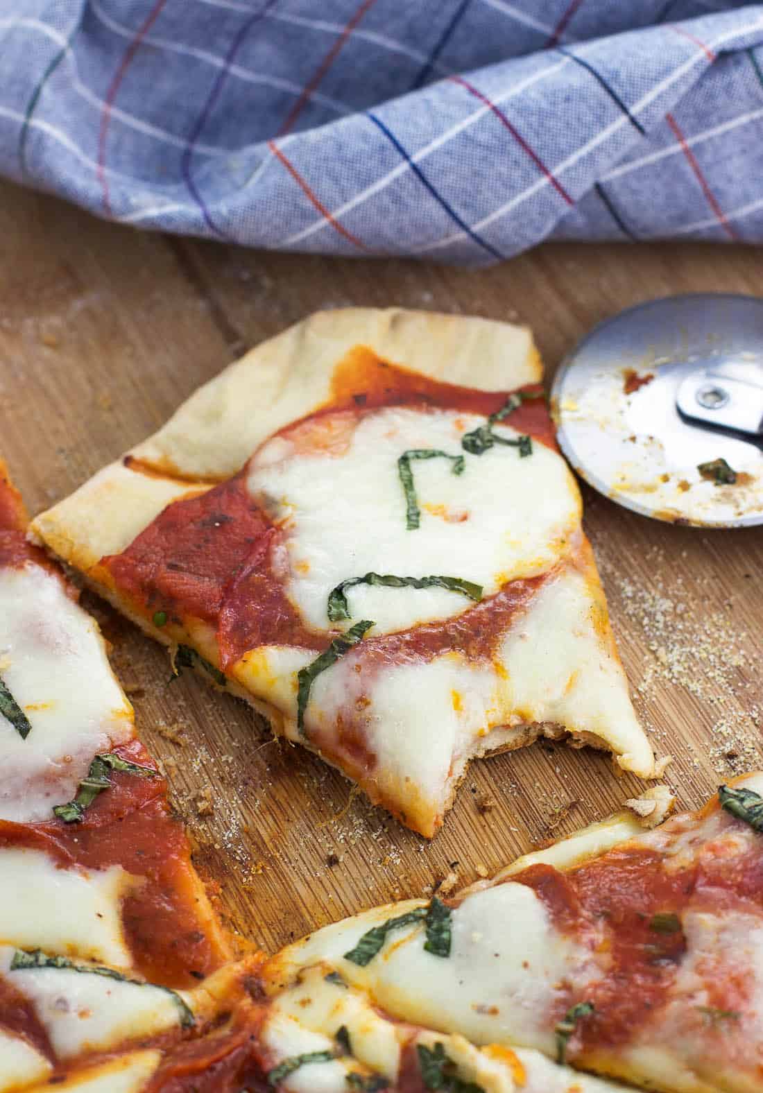 A slice of pizza on a wooden board with a bite taken out of it.