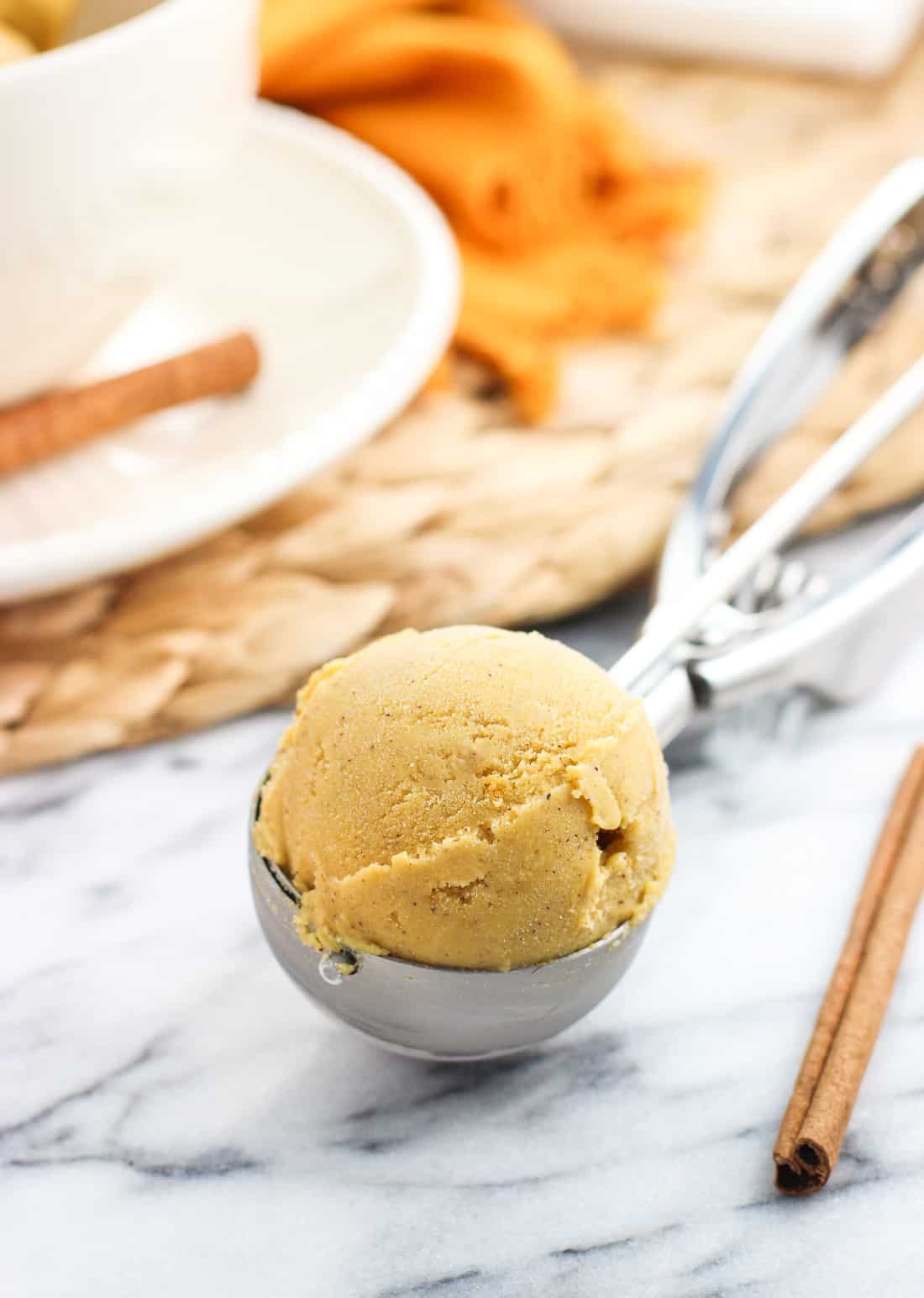 A rounded scoop of pumpkin ice cream in a metal kitchen scoop