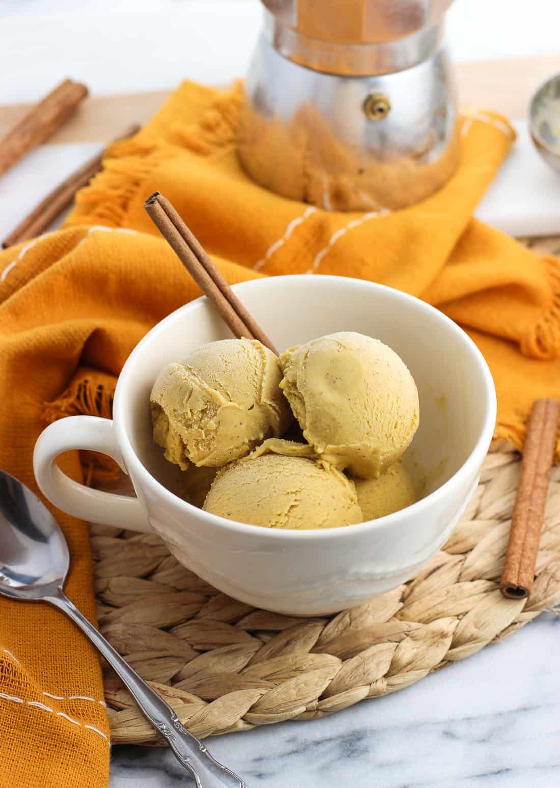 Pumpkin gelato affogato in a large ceramic mug next to a spoon and a small pot of espresso