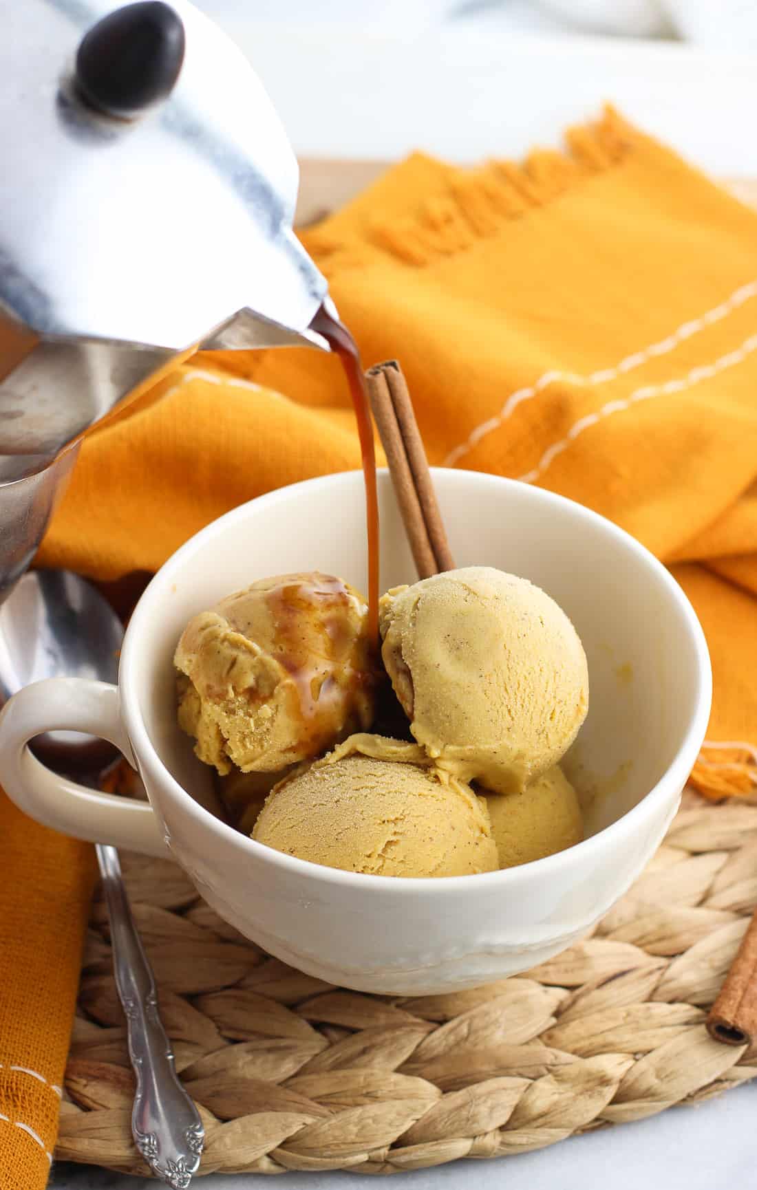 Four small scoops of pumpkin gelato in a large mug with espresso being poured over top, all garnished with a whole cinnamon stick