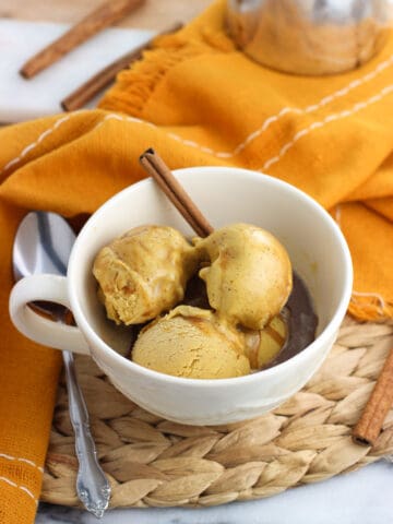 Four small scoops of pumpkin gelato in a large mug with espresso poured over top, all garnished with a whole cinnamon stick