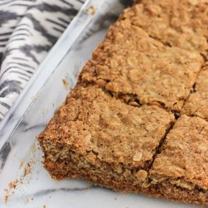 A glass pan of oatmeal bars sliced into squares next to a linen dish towel