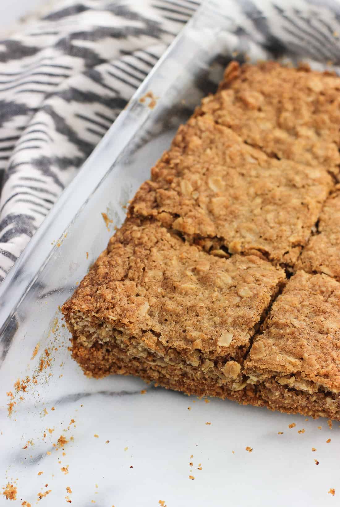 A glass pan of oatmeal bars sliced into squares next to a linen dish towel