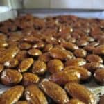 A single layer of gingerbread roasted almonds on a sheet pan.