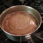 Hot chocolate mixture frothed in a saucepan on the stove top.