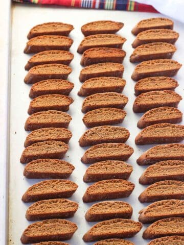 Lined up gingerbread biscotti on a metal cookie sheet.