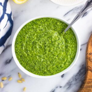 A bowl of spinach pesto with a spoon in it.
