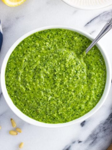 A bowl of spinach pesto with a spoon in it.