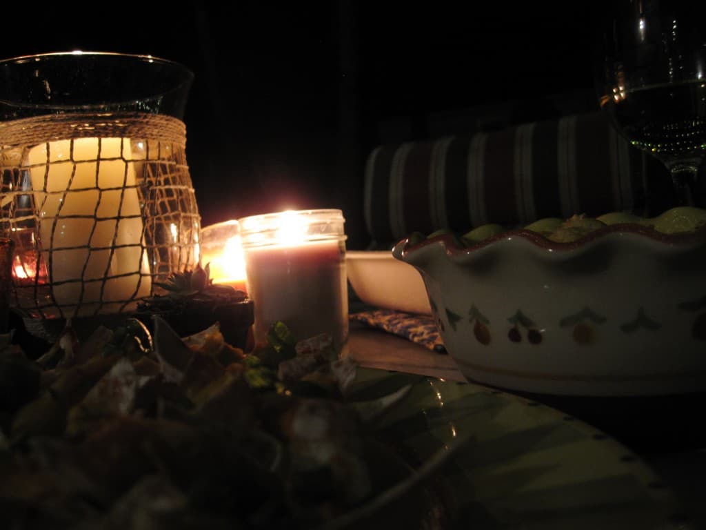 An outdoor tablescape including a lit candle, a salad, and serving bowls.