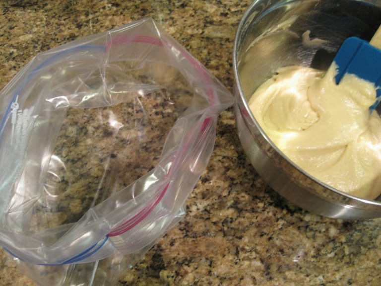 An open zip-top bag next to a metal mixing bowl with donut batter in it.