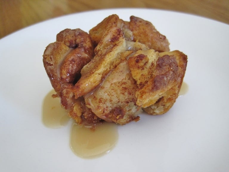 A cinnamon roll baked in a muffin tin on a plate with maple syrup.