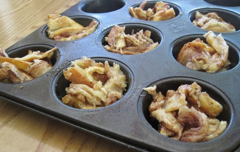 Ripped up cinnamon rolls in a muffin tin.