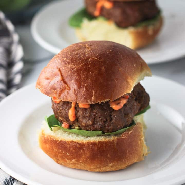 A turkey burger slider, with lettuce and chili garlic sauce, on a small slider bun on a plate with another in the background