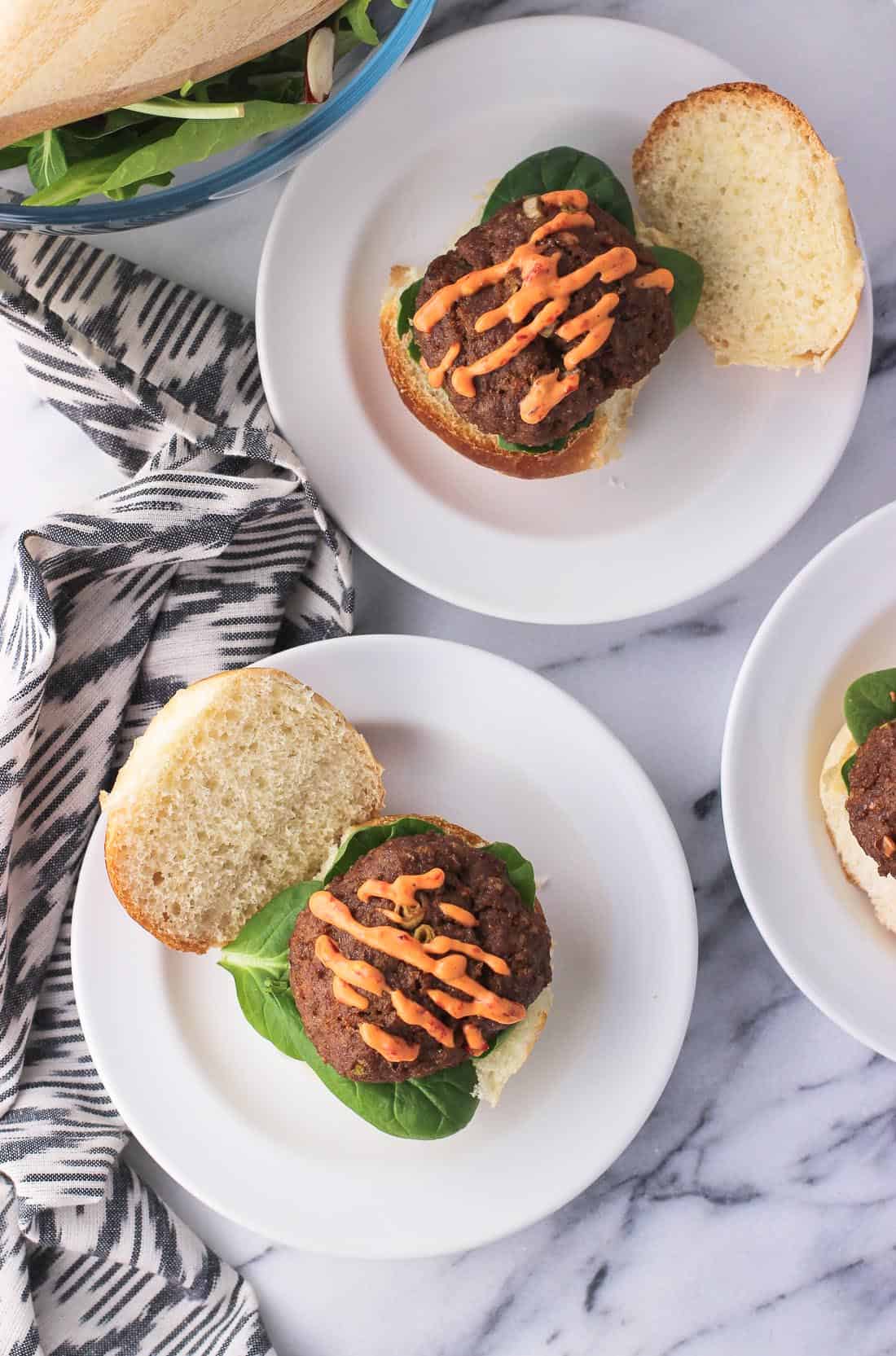 An overhead shot of open-face sliders on small plates, showing the drizzle of chili garlic sauce on each turkey patty