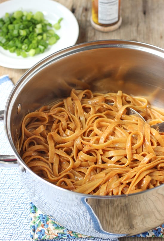 Almond butter noodles in a large metal pot with a serving spoon.