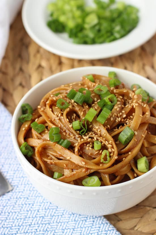 A bowl of almond butter noodles garnished with sesame seeds and sliced green onion. 