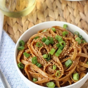 A bowl of almond butter noodles garnished with sliced green onion and sesame seeds.