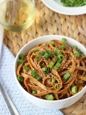 A bowl of almond butter noodles garnished with sliced green onion and sesame seeds.
