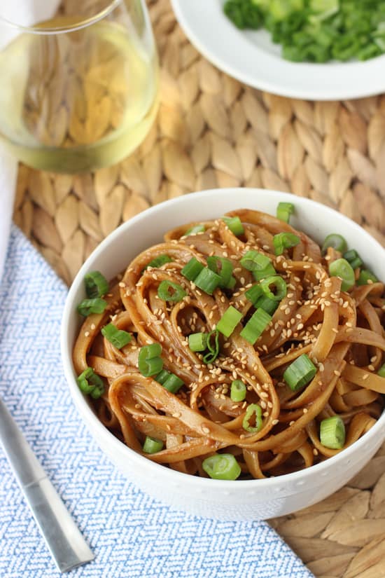 A bowl of almond butter noodles garnished with sliced green onion and sesame seeds.