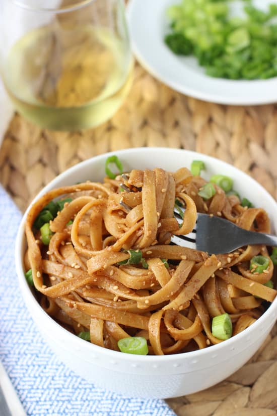 A fork twirled around almond butter noodles in a bowl.