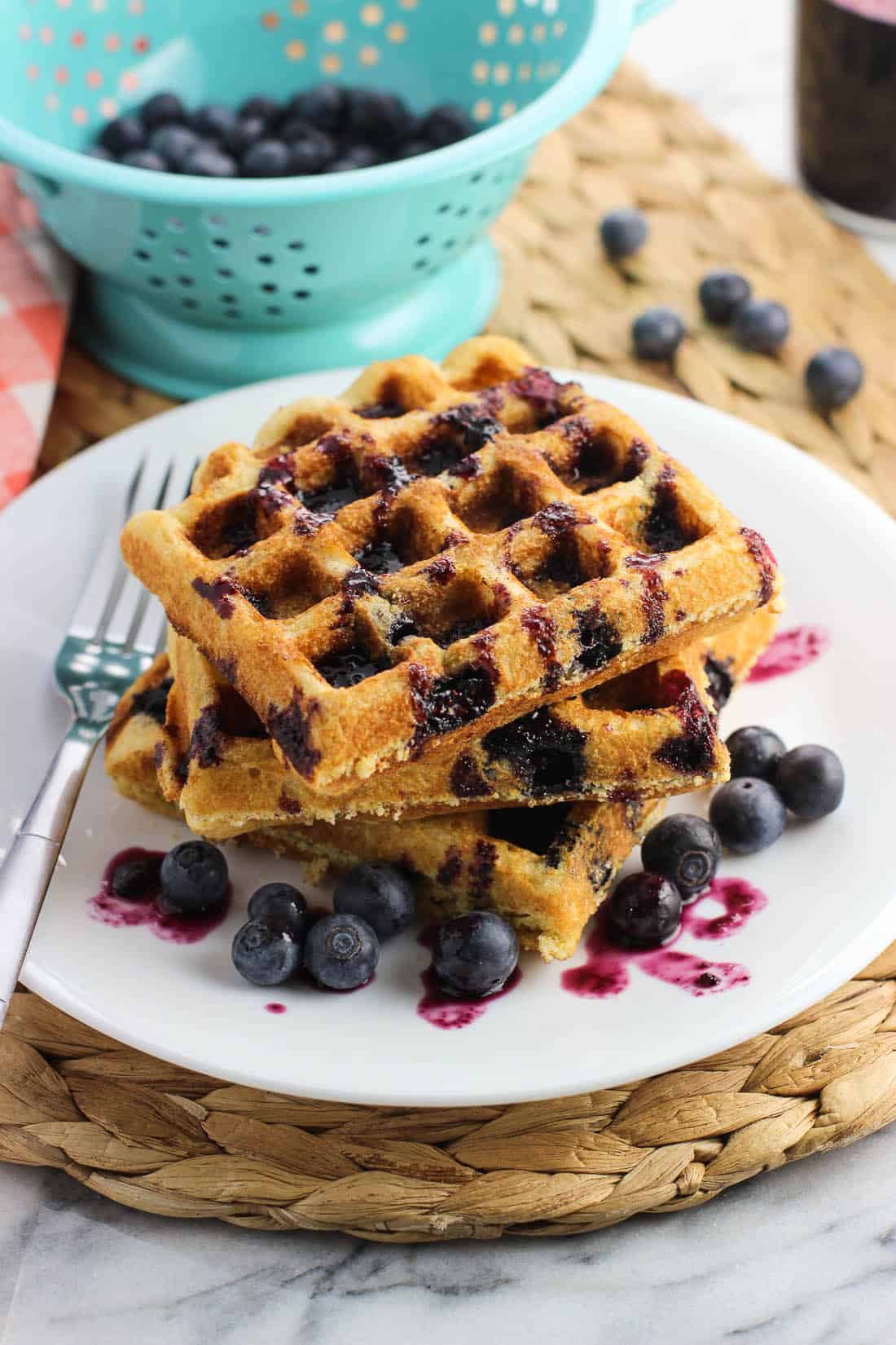 A stack of three blueberry cornbread waffles drizzled with syrup on a plate with a fork.