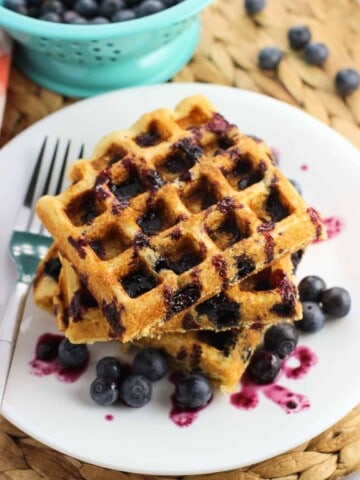 Three waffles on a plate with fresh blueberries and drizzled with blueberry maple syrup