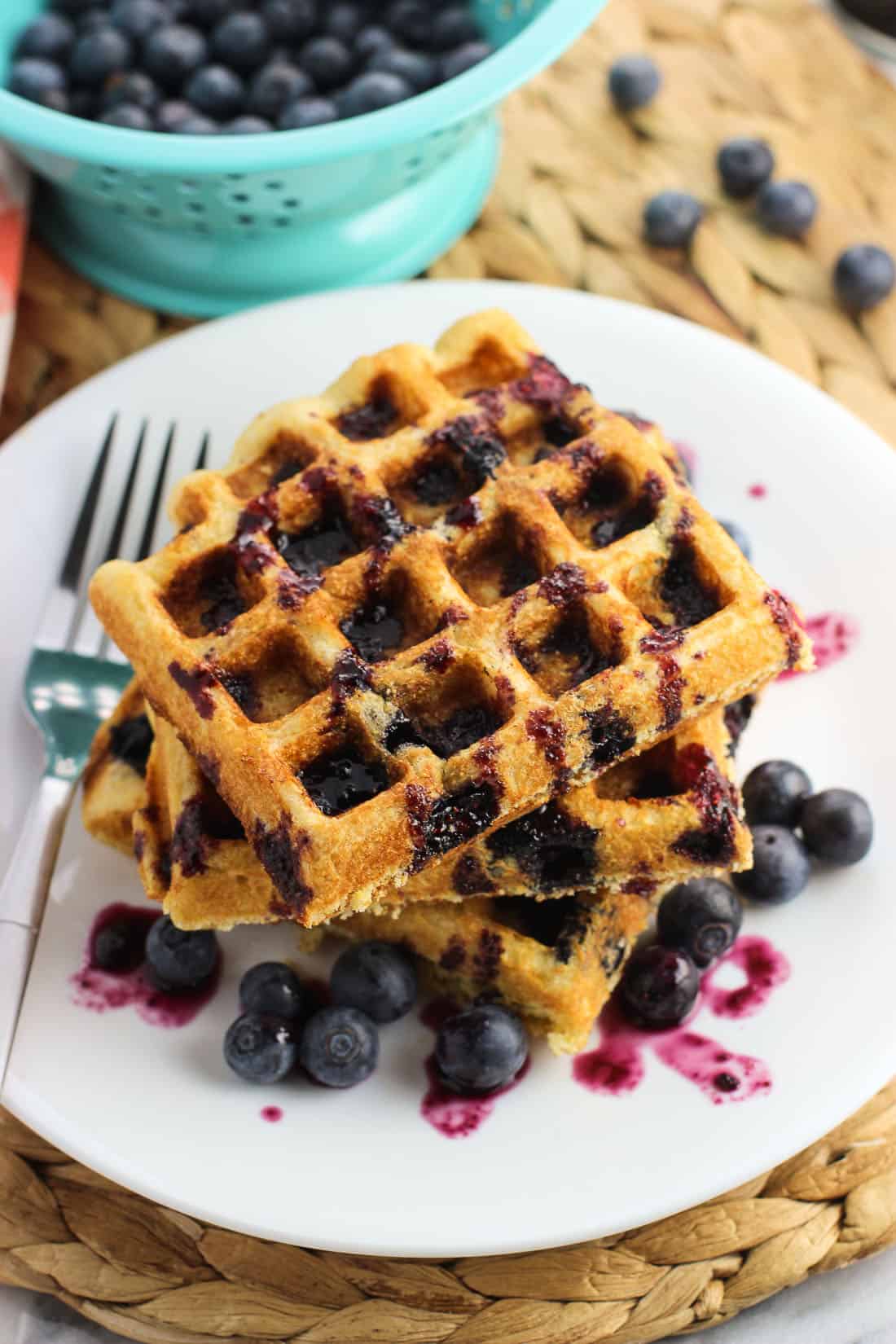 Three waffles on a plate drizzled with syrup and served with plenty of fresh berries.