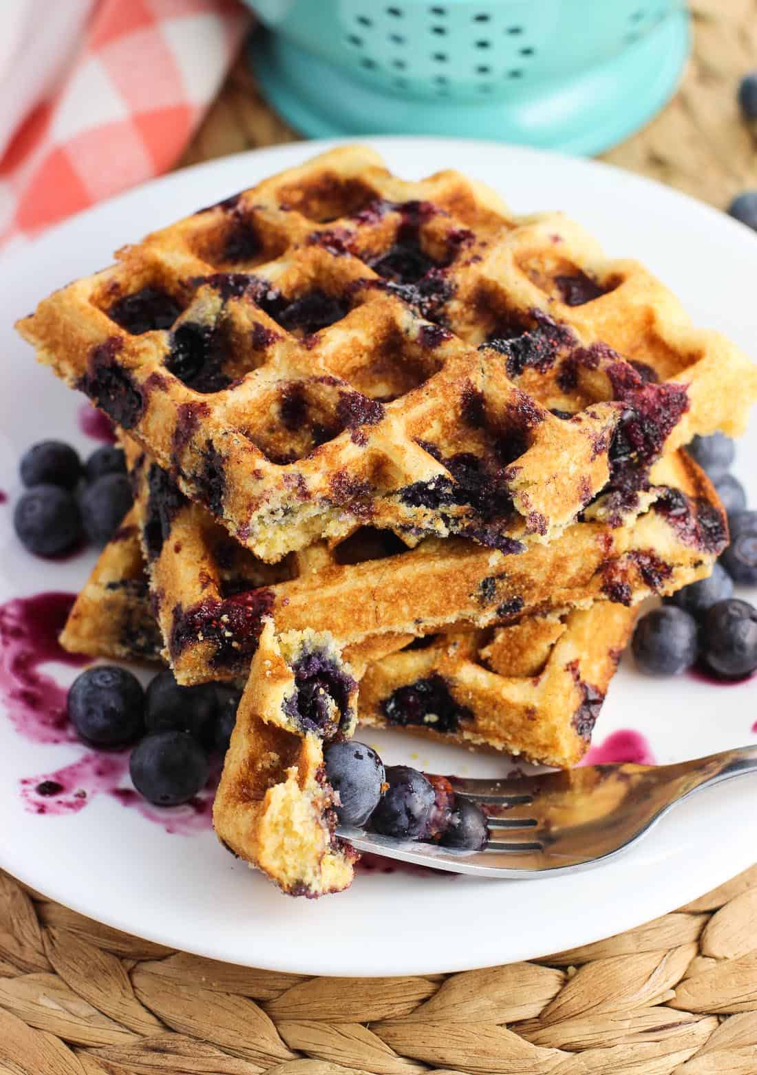 Three waffles on a plate with a forkful of blueberries and a bite of waffle in the front