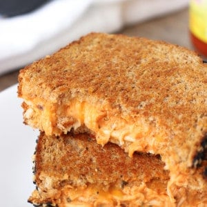 Two halves of a buffalo grilled cheese sandwich stacked on top of each other, with a big bite taken out of the top sandwich half