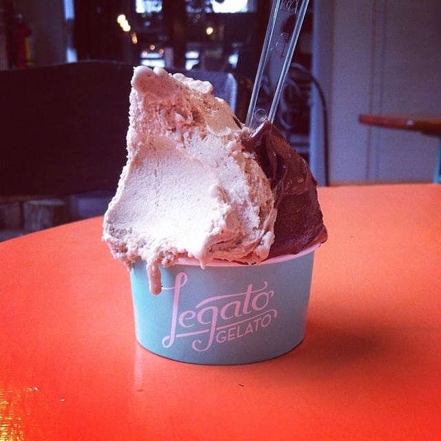 An over-flowing cup of gelato on a table with a plastic spoon in it.