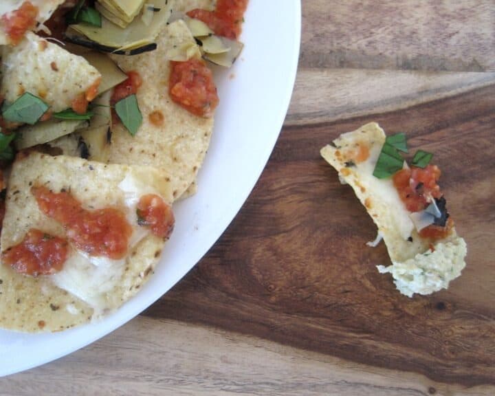 A tortilla covered with cheese, tomatoes, and basil pulled away from the plate of nachos.