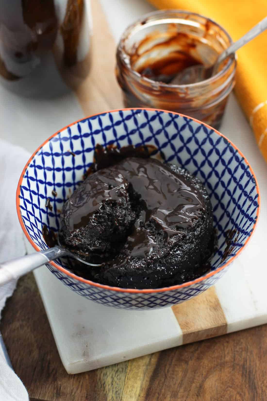 A spoon dug into a mug cake in a bowl topped with hot fudge