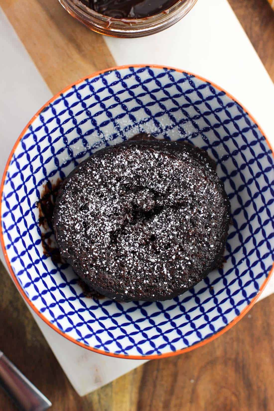 An overhead shot of a chocolate mug cake in a bowl dusted with confectioners' sugar