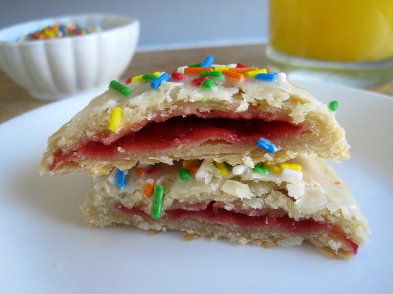 A pop tart on a plate cut in half to show the strawberry filling.