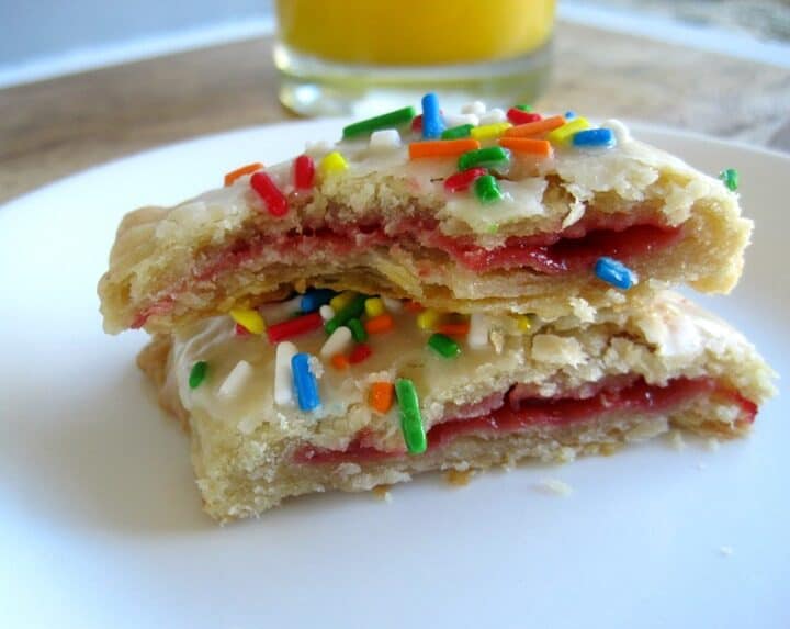 A pop tart on a plate cut in half to show the strawberry filling with a bite taken out of it.