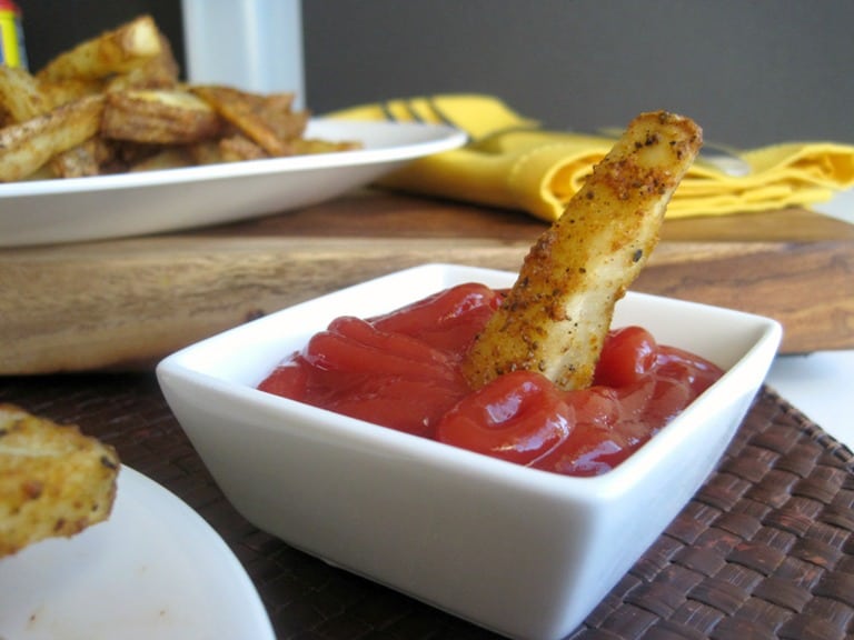 A potato wedge dunked into a small bowl of ketchup.