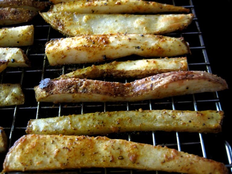 Seasoned potato wedges lined up on a wire rack after baking.