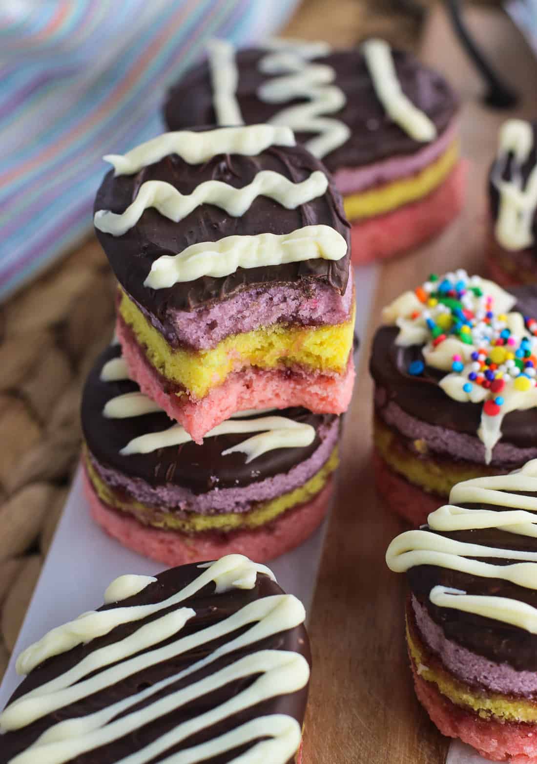 Easter egg rainbow cookies stacked on top of one another with a bite taken out of the top cookie.