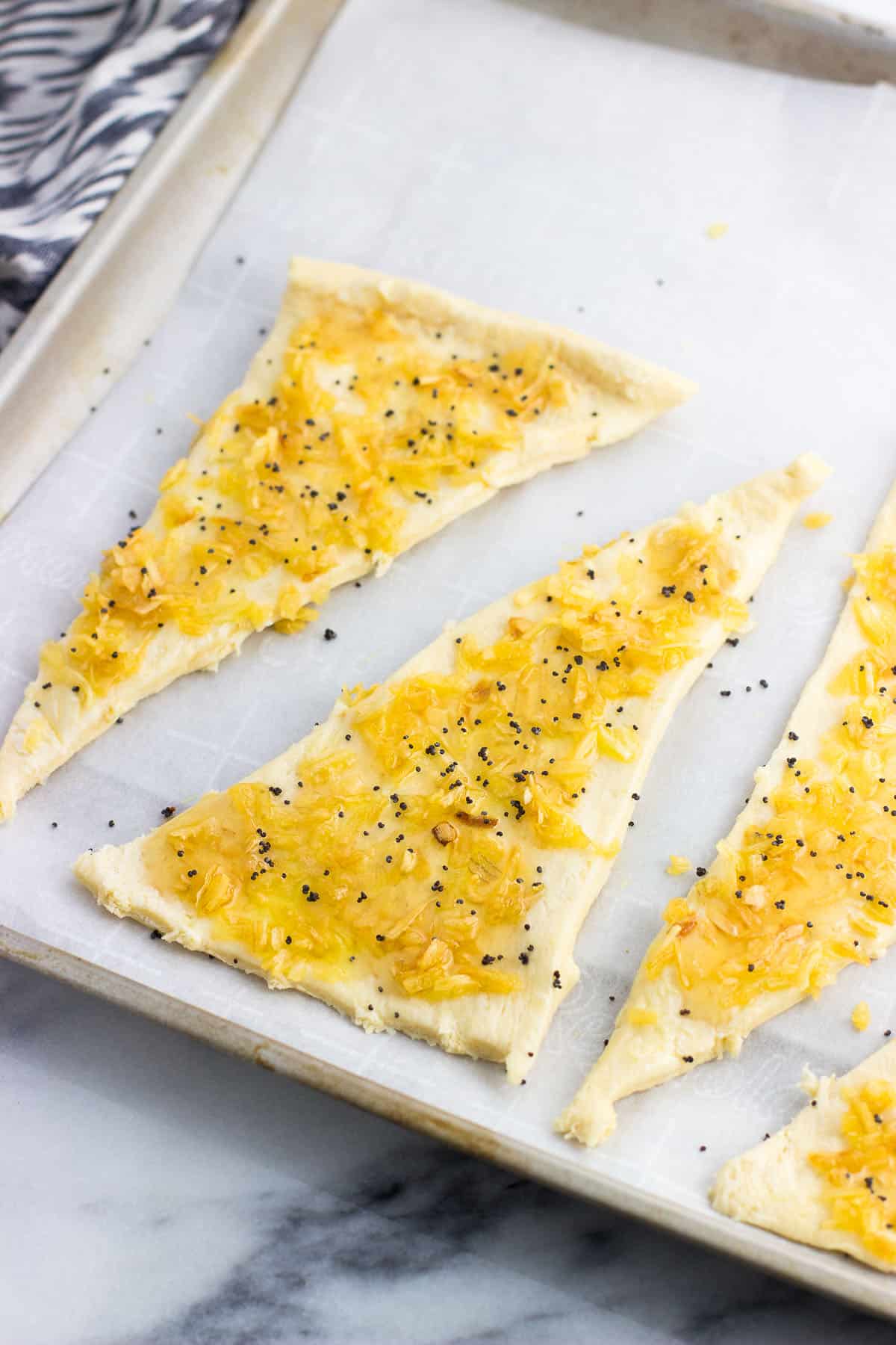 Onion filling spread onto crescent roll segments on a parchment lined baking sheet