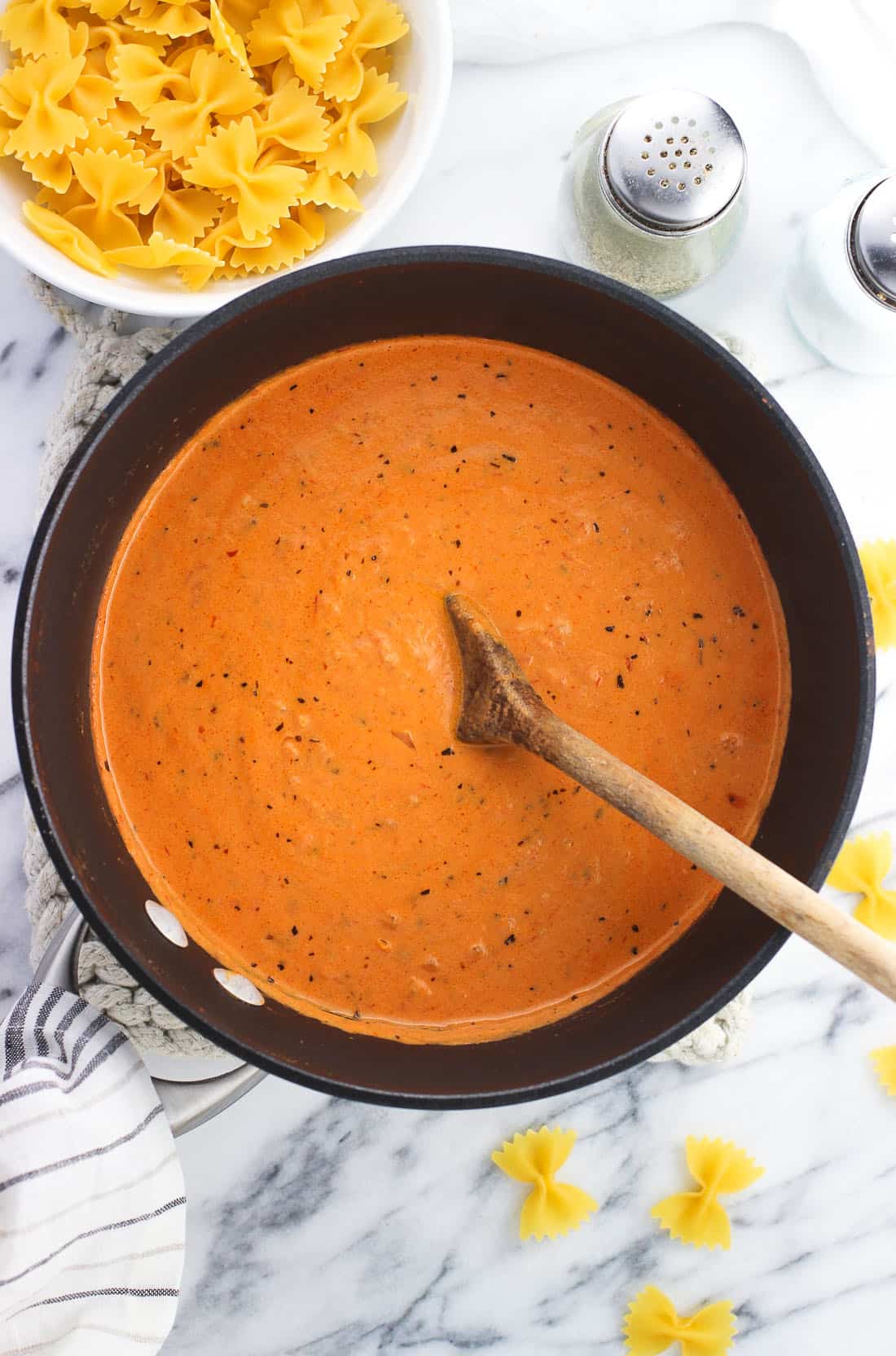 A sauce pan of vodka sauce surrounded by dry pasta and salt and pepper shakers.