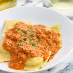 A dinner plate of ravioli and vodka sauce garnished with fresh basil.