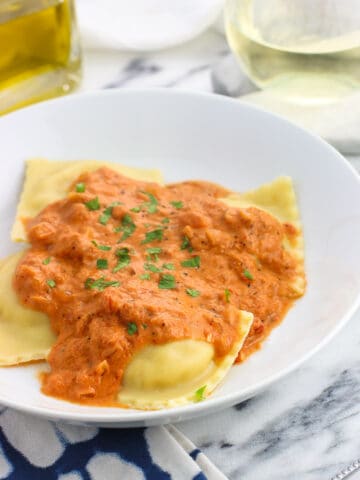 A dinner plate of ravioli and vodka sauce garnished with fresh basil.