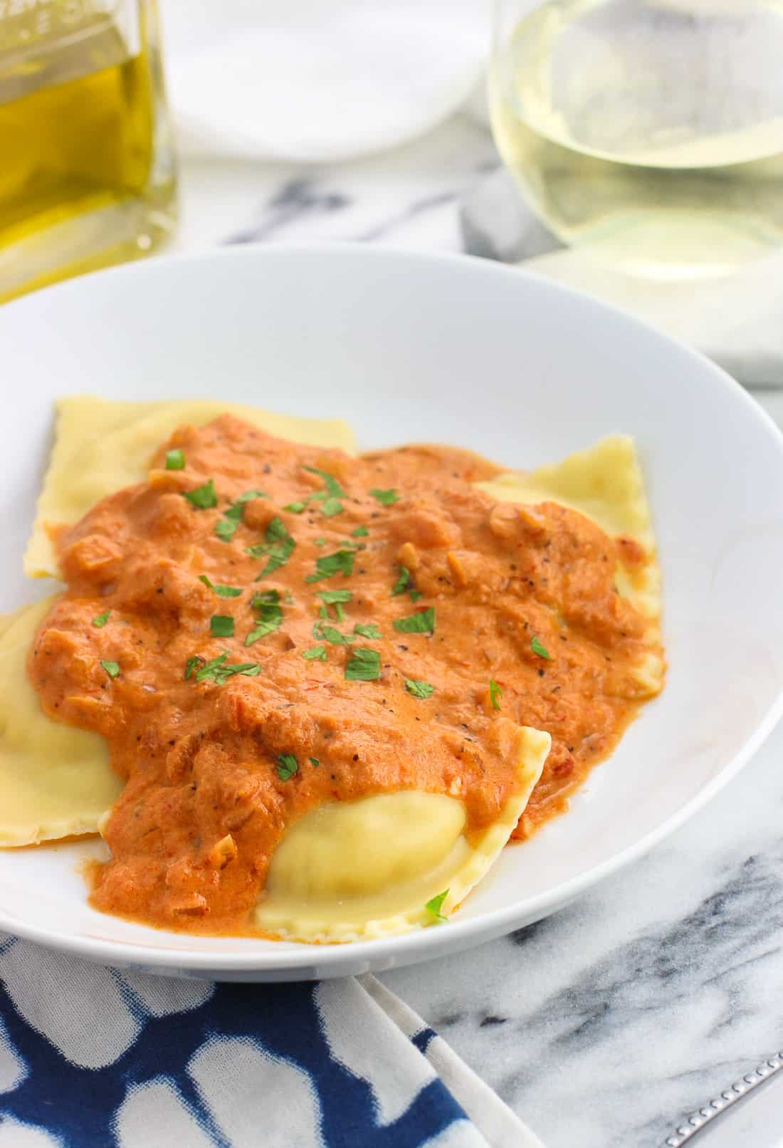 A dinner plate of ravioli and vodka sauce garnished with fresh basil.