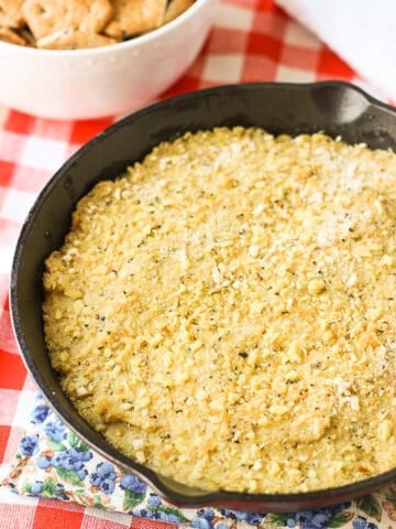 Baked stuffed artichoke dip in a round cast iron skillet next to a bowl of crackers.