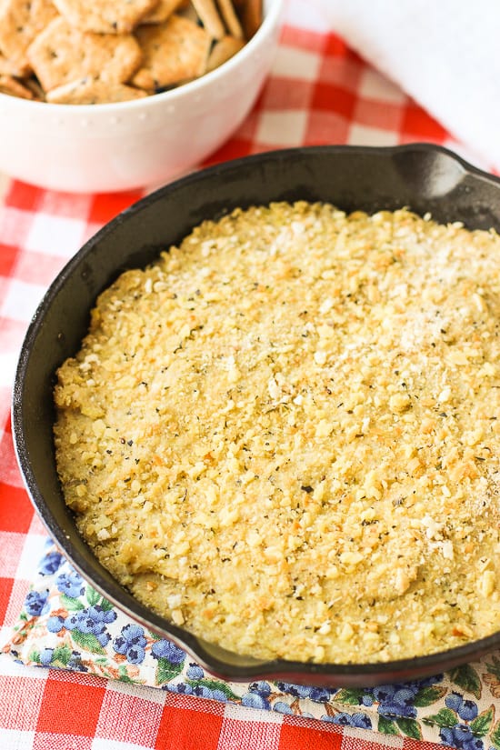 Baked stuffed artichoke dip in a round cast iron skillet next to a bowl of crackers.