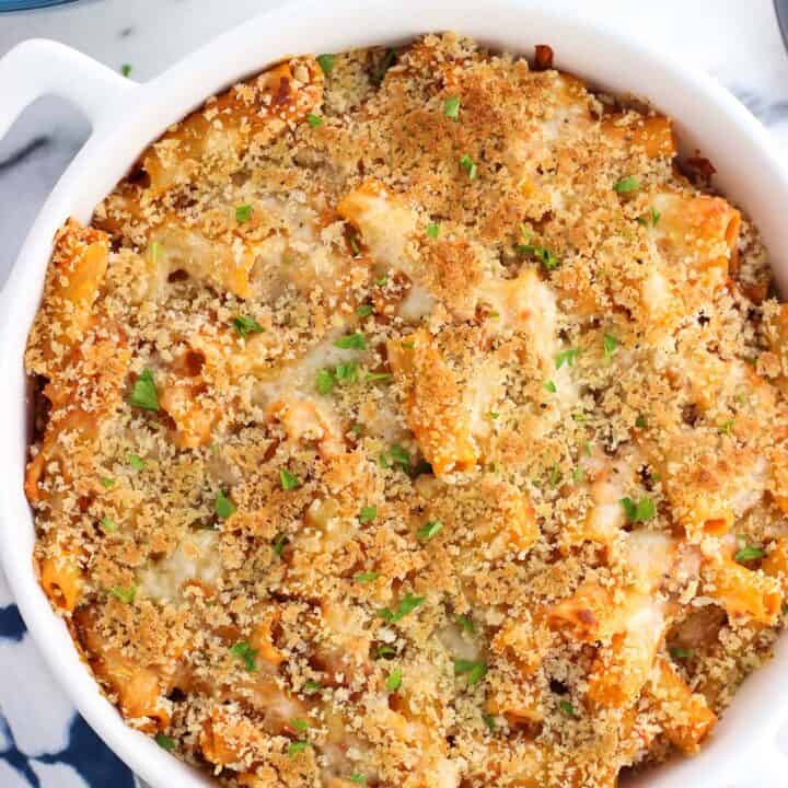 A round ceramic dish filled with baked pasta and topped with a layer of crispy panko.