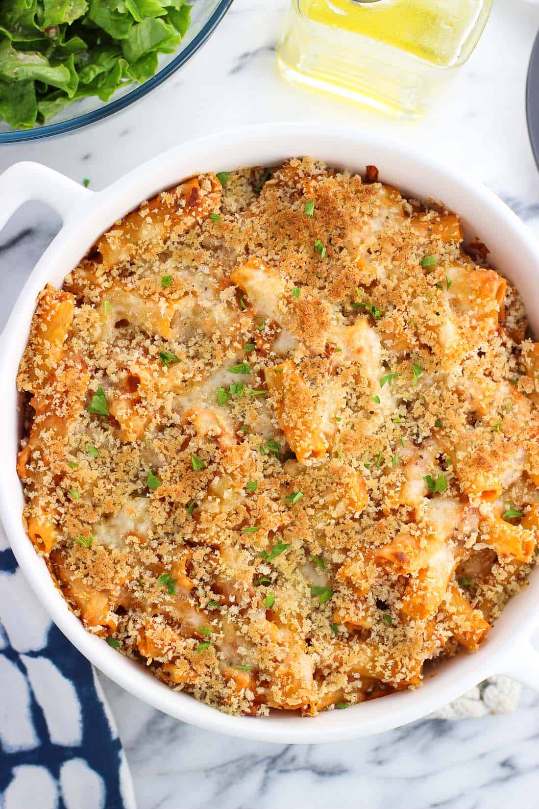 A round ceramic dish filled with baked pasta and topped with a layer of crispy panko.